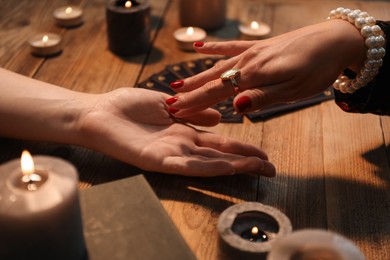 Fortune teller reading lines on woman's palm at wooden table, closeup. Chiromancy