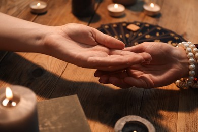 Photo of Fortune teller reading lines on woman's palm at wooden table, closeup. Chiromancy