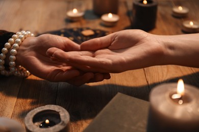 Photo of Fortune teller reading lines on woman's palm at wooden table, closeup. Chiromancy