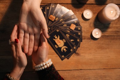 Photo of Fortune teller reading lines on woman's palm at wooden table, top view. Chiromancy