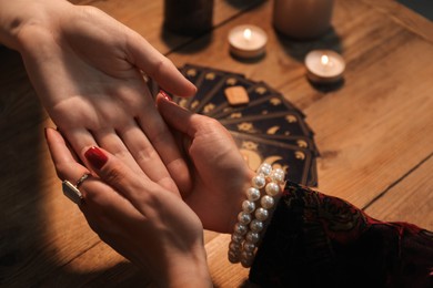 Photo of Fortune teller reading lines on woman's palm at wooden table, closeup. Chiromancy