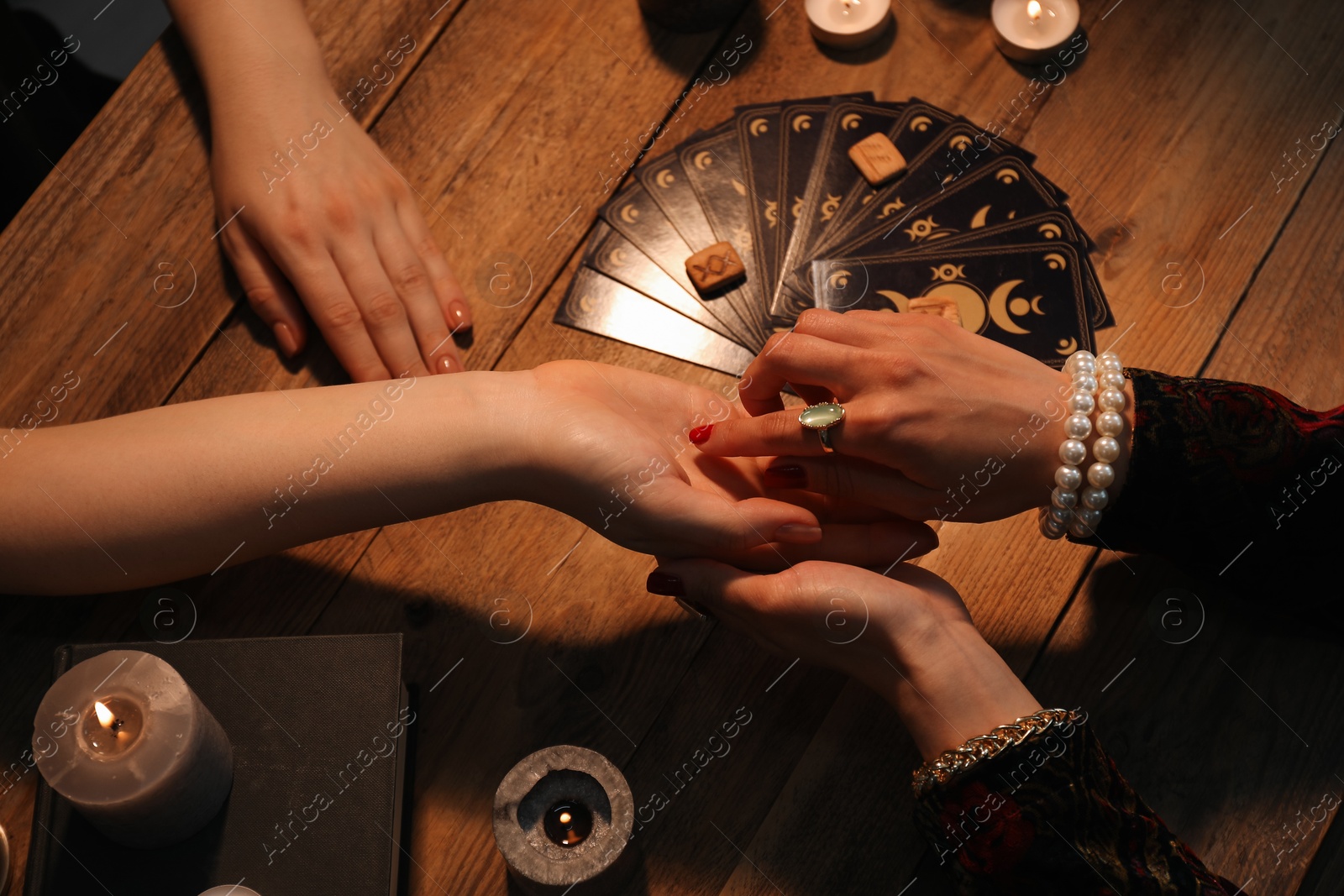 Photo of Fortune teller reading lines on woman's palm at wooden table, closeup. Chiromancy