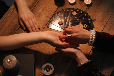 Fortune teller reading lines on woman's palm at wooden table, closeup. Chiromancy