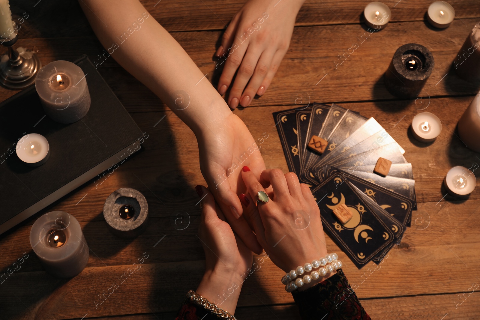 Photo of Fortune teller reading lines on woman's palm at wooden table, top view. Chiromancy