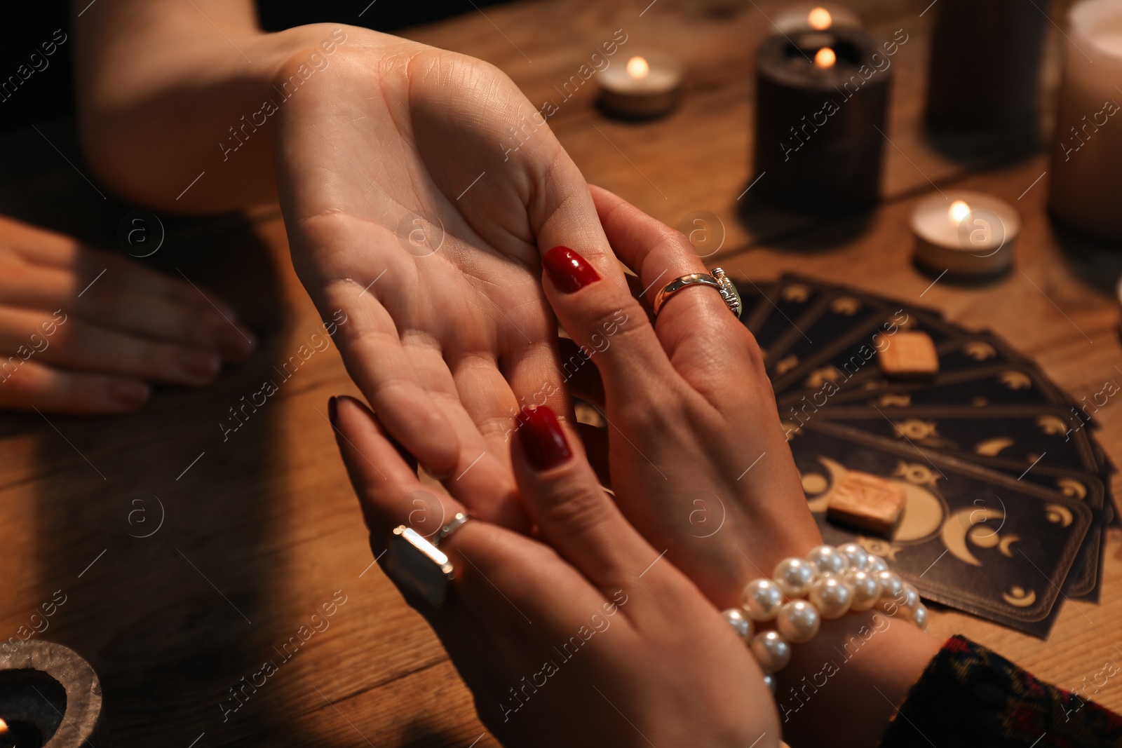 Photo of Fortune teller reading lines on woman's palm at wooden table, closeup. Chiromancy