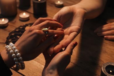 Fortune teller reading lines on woman's palm at wooden table, closeup. Chiromancy