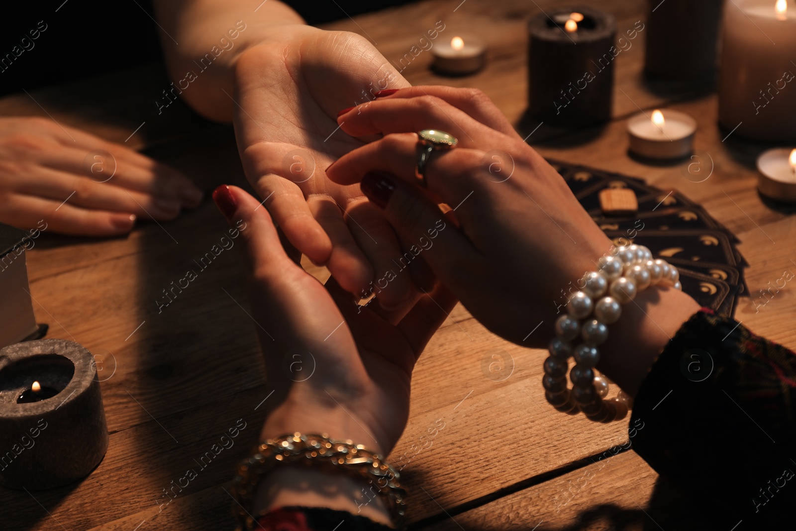 Photo of Fortune teller reading lines on woman's palm at wooden table, closeup. Chiromancy