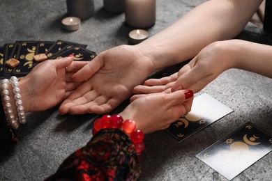 Photo of Fortune teller reading lines on woman's palm at black table, closeup. Chiromancy