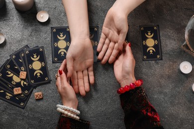 Fortune teller reading lines on woman's palm at grey table, top view. Chiromancy