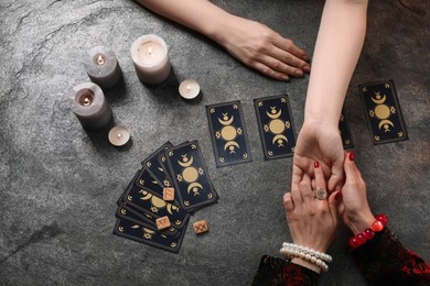 Fortune teller reading lines on woman's palm at grey table, top view. Chiromancy