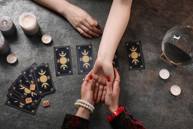 Fortune teller reading lines on woman's palm at grey table, top view. Chiromancy