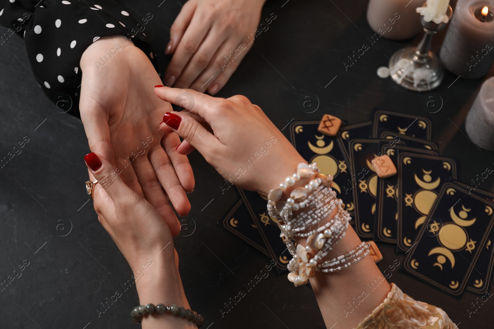 Photo of Fortune teller reading lines on woman's palm at black table, closeup. Chiromancy