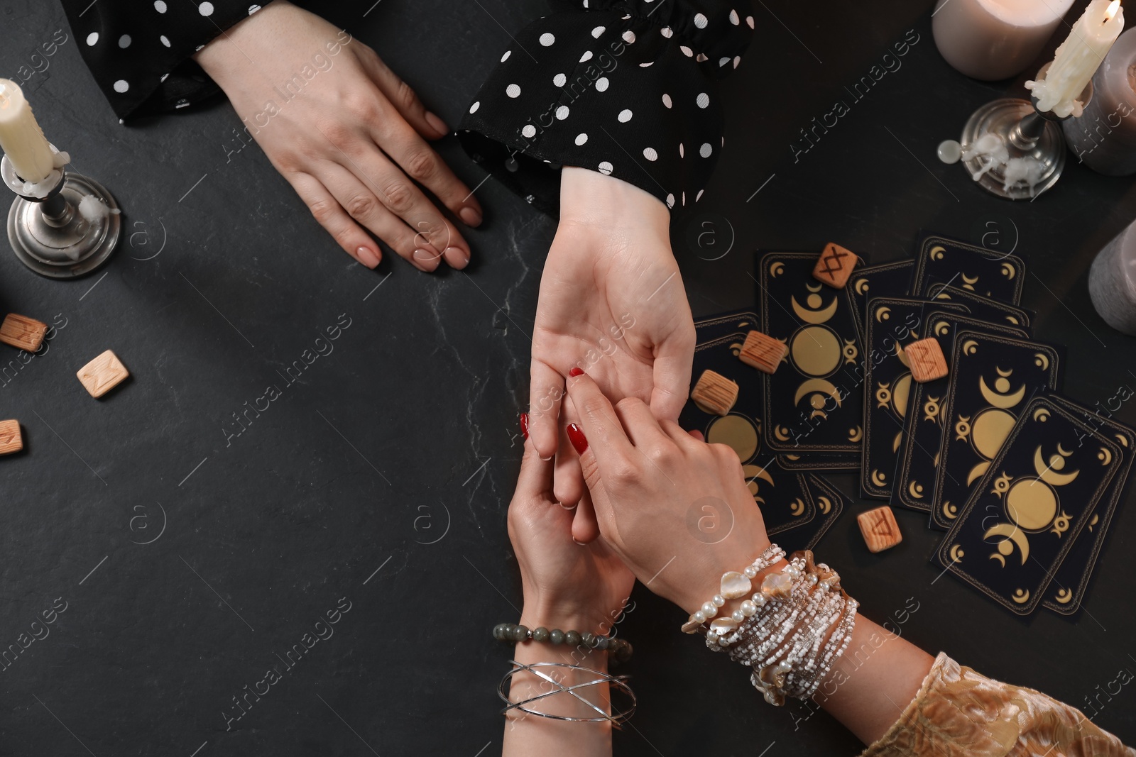 Photo of Fortune teller reading lines on woman's palm at black table, top view. Chiromancy