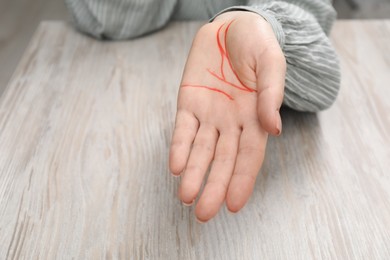 Photo of Woman showing palm with drawn lines at white wooden table, closeup. Chiromancy and foretelling