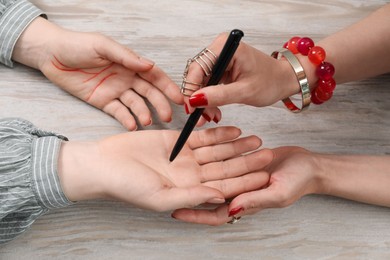 Fortune teller reading lines on woman's palm at wooden table, closeup. Chiromancy