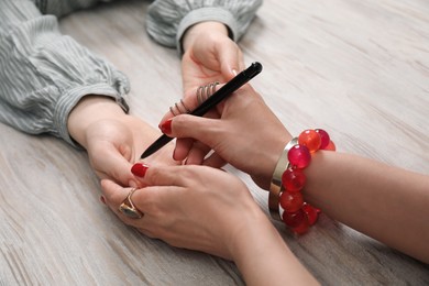 Photo of Fortune teller reading lines on woman's palm at wooden table, closeup. Chiromancy