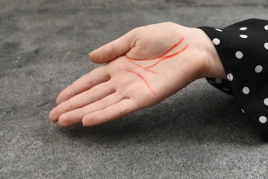 Photo of Woman showing palm with drawn lines at grey table, closeup. Chiromancy and foretelling