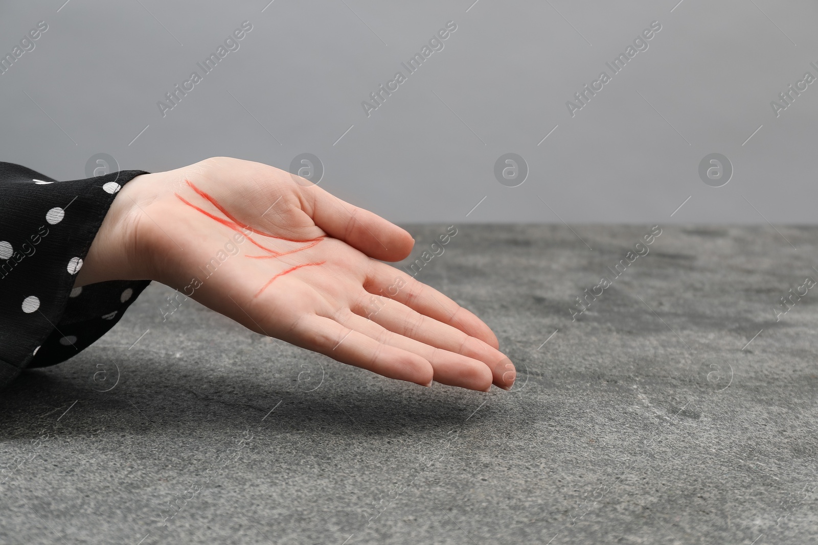 Photo of Chiromancy and foretelling. Woman showing palm with drawn lines at grey table, closeup. Space for text