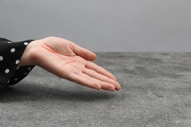 Chiromancy and foretelling. Woman showing palm with drawn lines at grey table, closeup. Space for text