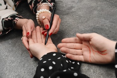 Photo of Fortune teller reading lines on woman's palm at grey table, closeup. Chiromancy