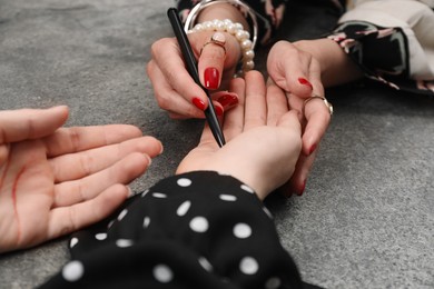 Fortune teller reading lines on woman's palm at grey table, closeup. Chiromancy