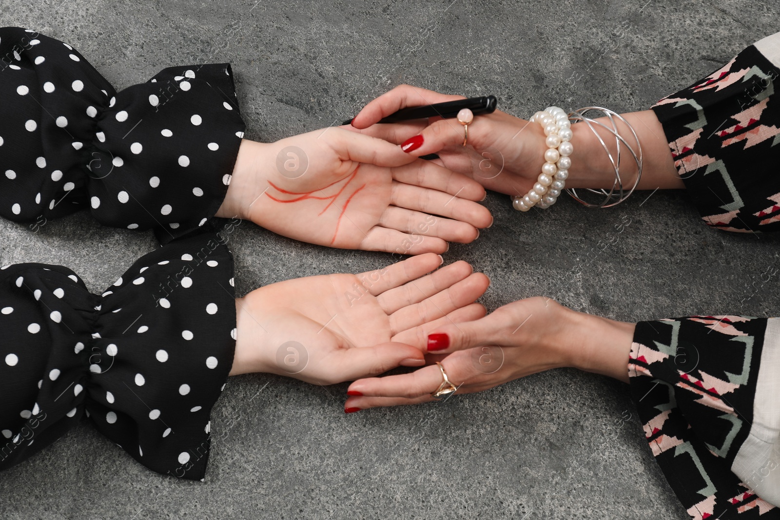 Photo of Fortune teller reading lines on woman's palm at grey table, top view. Chiromancy