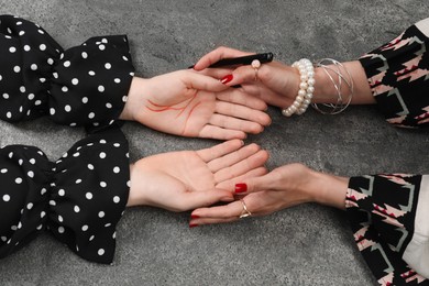 Fortune teller reading lines on woman's palm at grey table, top view. Chiromancy