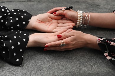 Fortune teller reading lines on woman's palm at grey table, closeup. Chiromancy