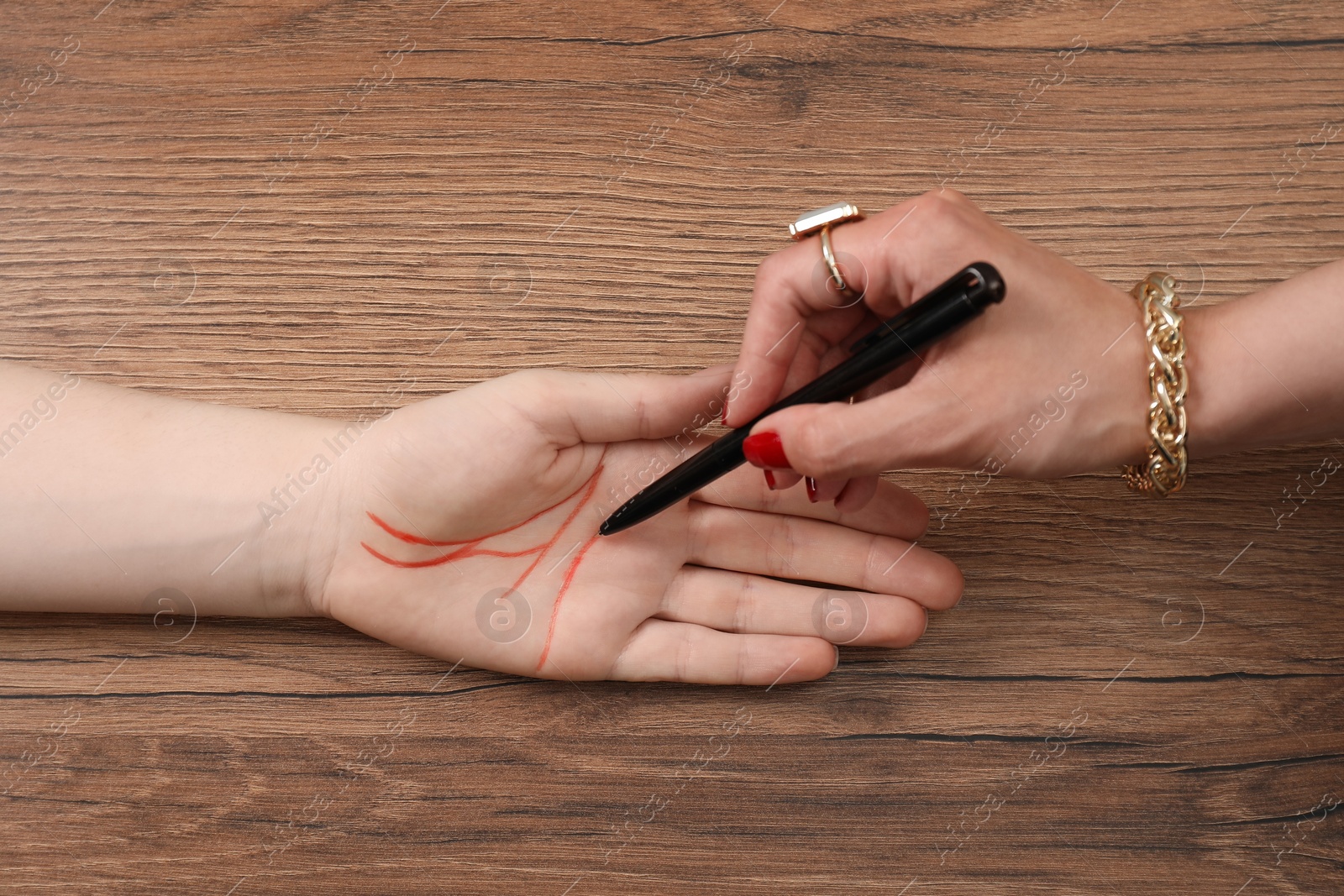 Photo of Fortune teller reading lines on woman's palm at wooden table, top view. Chiromancy