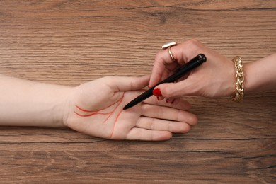 Photo of Fortune teller reading lines on woman's palm at wooden table, top view. Chiromancy