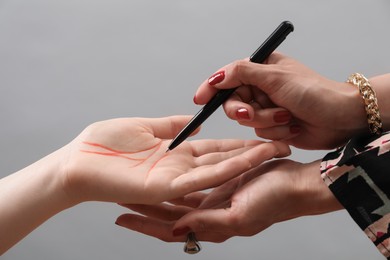 Fortune teller reading lines on woman's palm against light grey background, closeup. Chiromancy