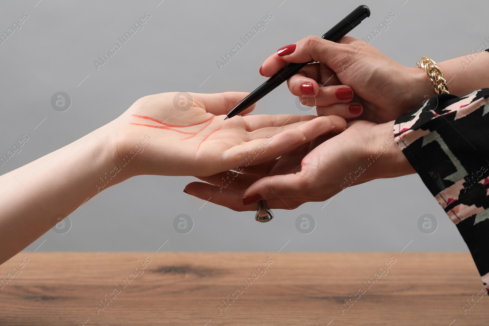 Photo of Fortune teller reading lines on woman's palm at wooden table, closeup. Chiromancy