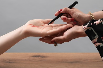 Photo of Fortune teller reading lines on woman's palm at wooden table, closeup. Chiromancy