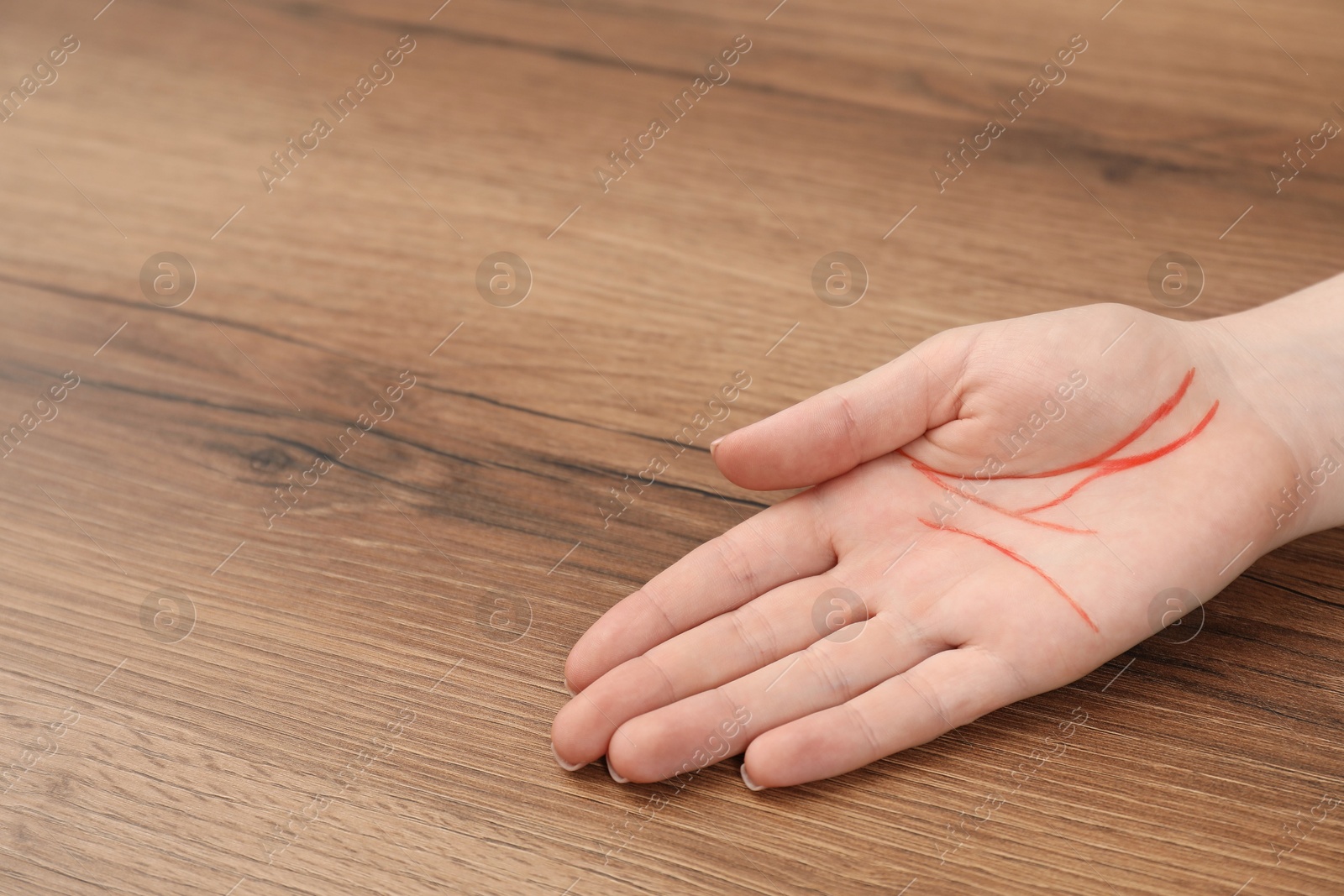 Photo of Chiromancy and foretelling. Woman showing palm with drawn lines at wooden table, closeup. Space for text