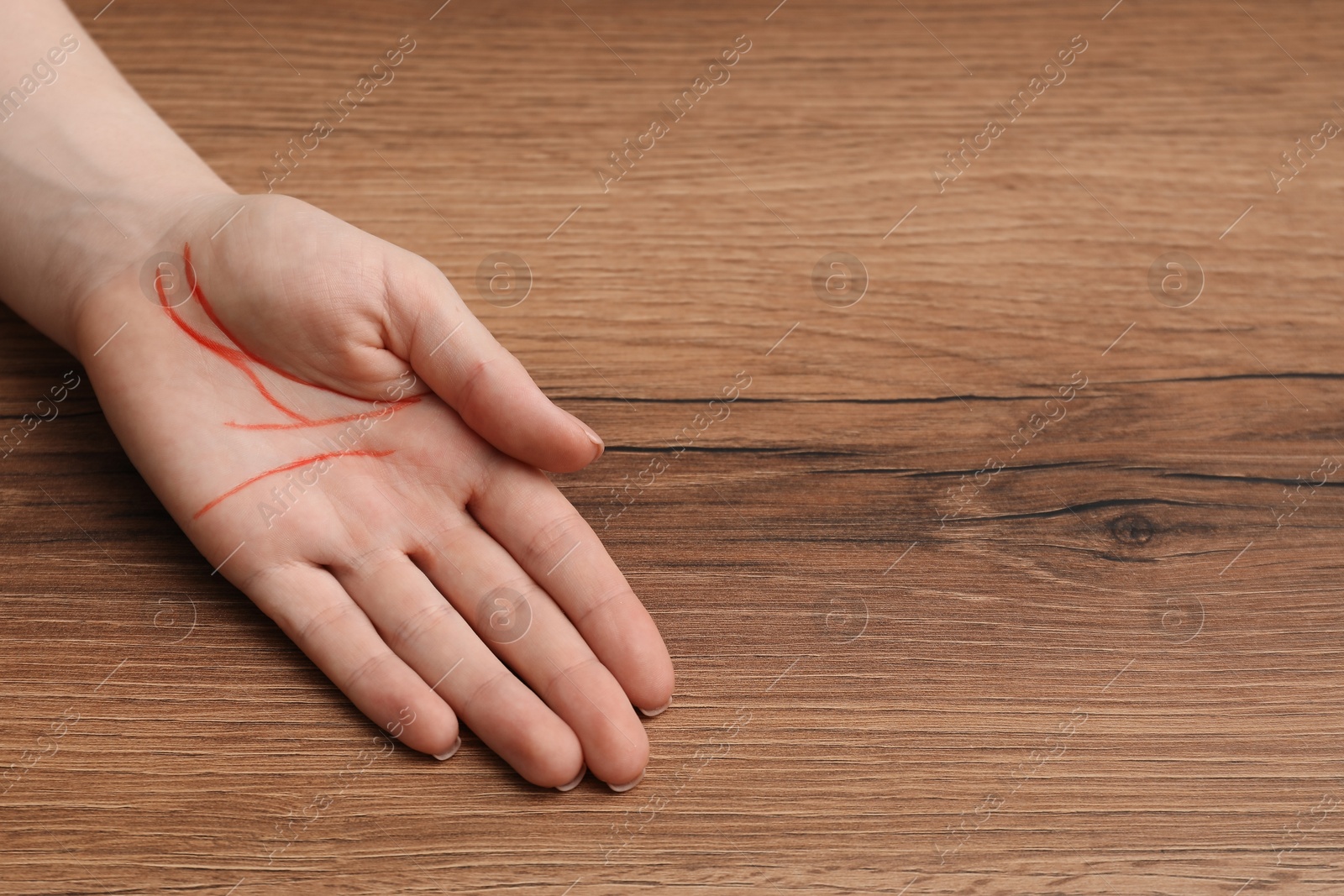 Photo of Chiromancy and foretelling. Woman showing palm with drawn lines at wooden table, closeup. Space for text