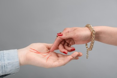 Photo of Fortune teller reading lines on woman's palm against light grey background, closeup. Chiromancy