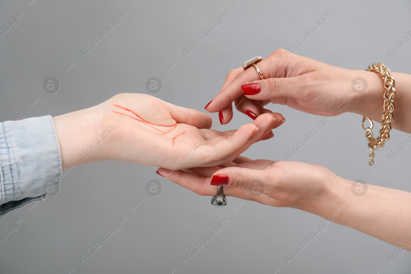 Photo of Fortune teller reading lines on woman's palm against light grey background, closeup. Chiromancy