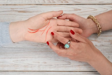 Fortune teller reading lines on woman's palm at white wooden table, top view. Chiromancy