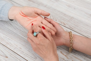 Fortune teller reading lines on woman's palm at white wooden table, closeup. Chiromancy