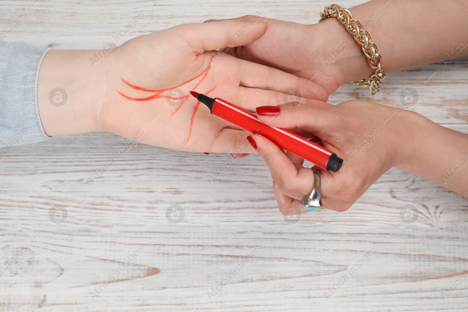 Photo of Fortune teller reading lines on woman's palm at white wooden table, top view. Chiromancy