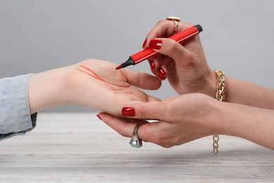 Fortune teller reading lines on woman's palm at white wooden table, closeup. Chiromancy