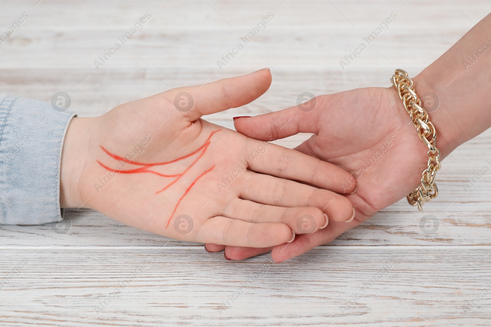 Photo of Fortune teller reading lines on woman's palm at white wooden table, closeup. Chiromancy