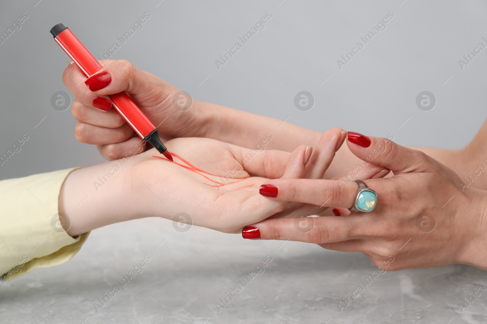 Photo of Fortune teller reading lines on woman's palm at grey table, closeup. Chiromancy