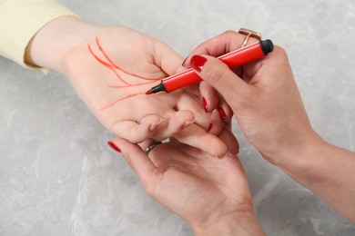 Fortune teller reading lines on woman's palm at grey table, closeup. Chiromancy