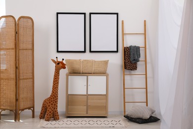 Photo of Child's room interior with modern furniture, toy giraffe and empty frames on wall