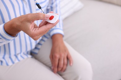 Photo of Senior woman pressing emergency call button at home, closeup. Space for text