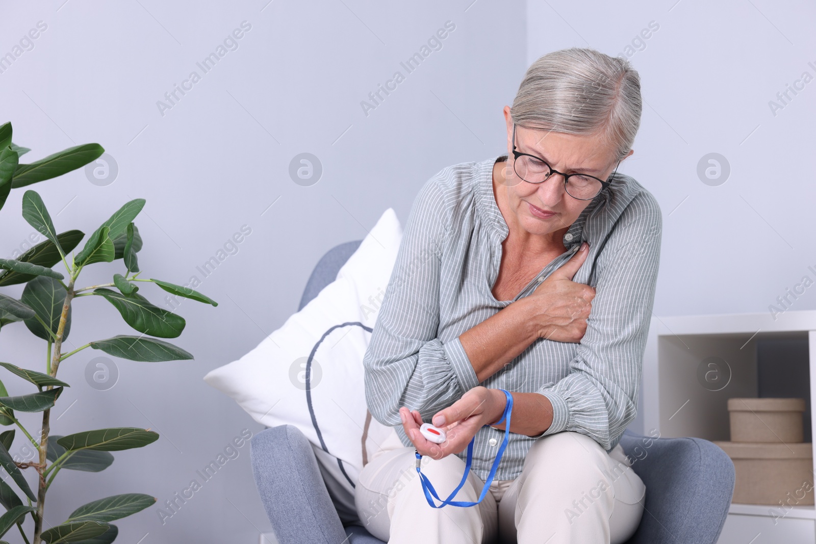 Photo of Senior woman suffering from heart pain holding emergency call button at home