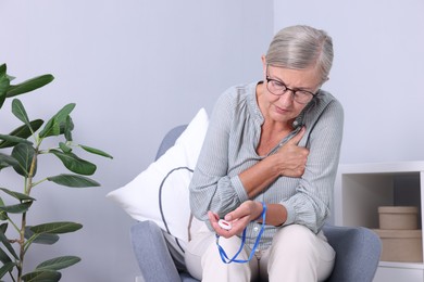 Senior woman suffering from heart pain holding emergency call button at home