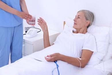 Senior woman with emergency call button taking glass of water nurse giving her in hospital, closeup