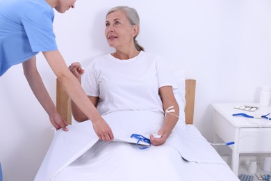 Nurse making patient's bed in a hospital, closeup. Senior woman with emergency call button indoors